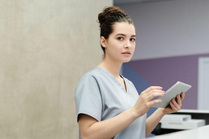 A clinic staff member in scrubs uses a tablet at the front desk