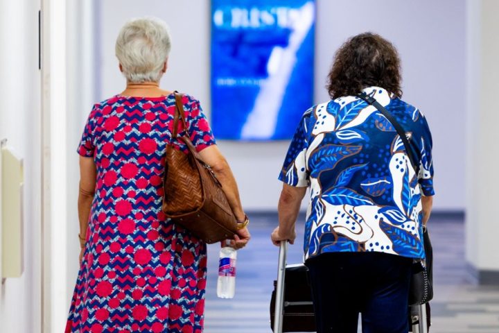 Two elderly patients walking down a hospital corridor, seen from behind